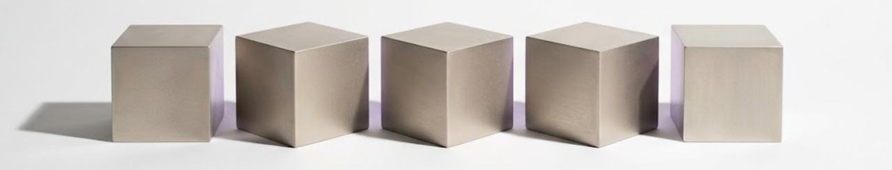 Five machined aluminium cubes in a row, each rotated further than the last
